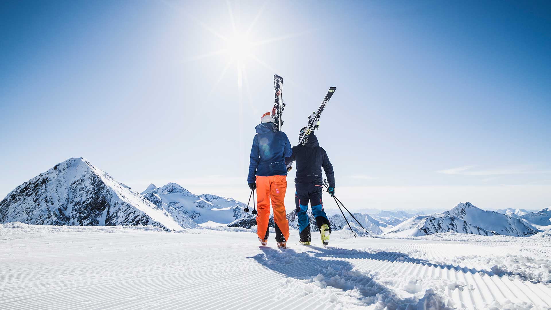 Zwei Skifahrer mit Skiern auf der Schulter genießen das sonnige Winterwetter während ihres Aktivurlaubs in den schneebedeckten Bergen Tirols.